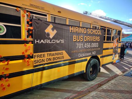 Yellow school bus with Harlow's banner advertising hiring for bus drivers. Includes phone number and 
