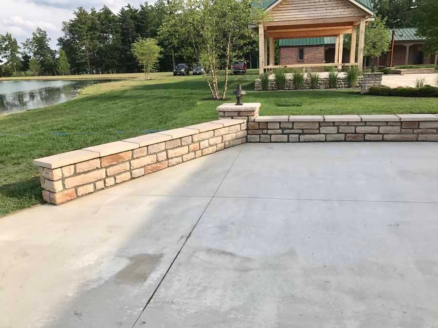 A concrete driveway with a brick wall and a gazebo in the background.