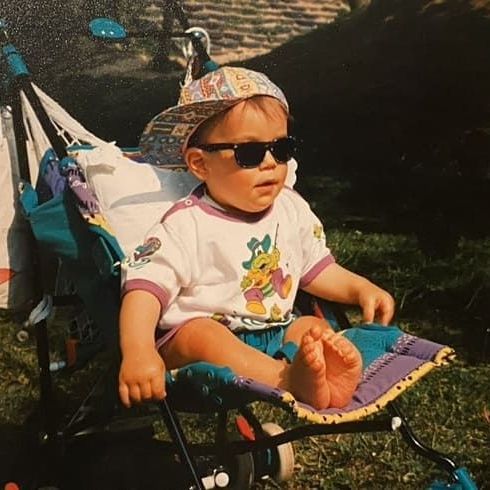 A baby wearing sunglasses and a hat is sitting in a stroller.