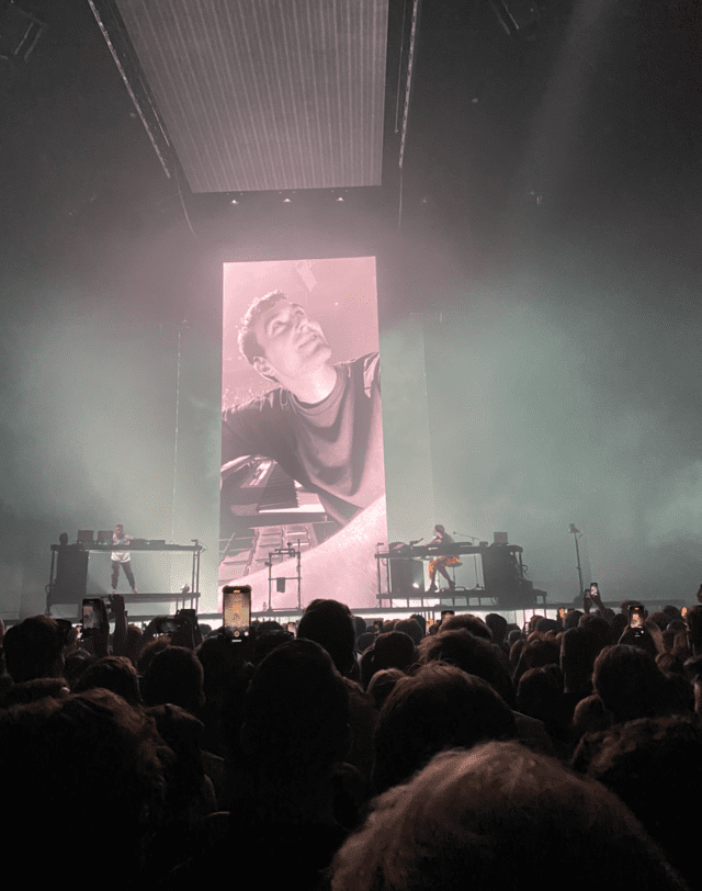 A crowd of people watching a concert with a large screen behind them