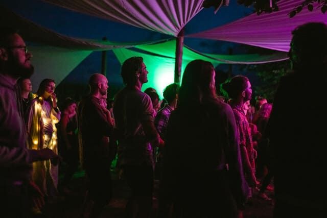 A group of people are dancing in a place with purple and green lights.