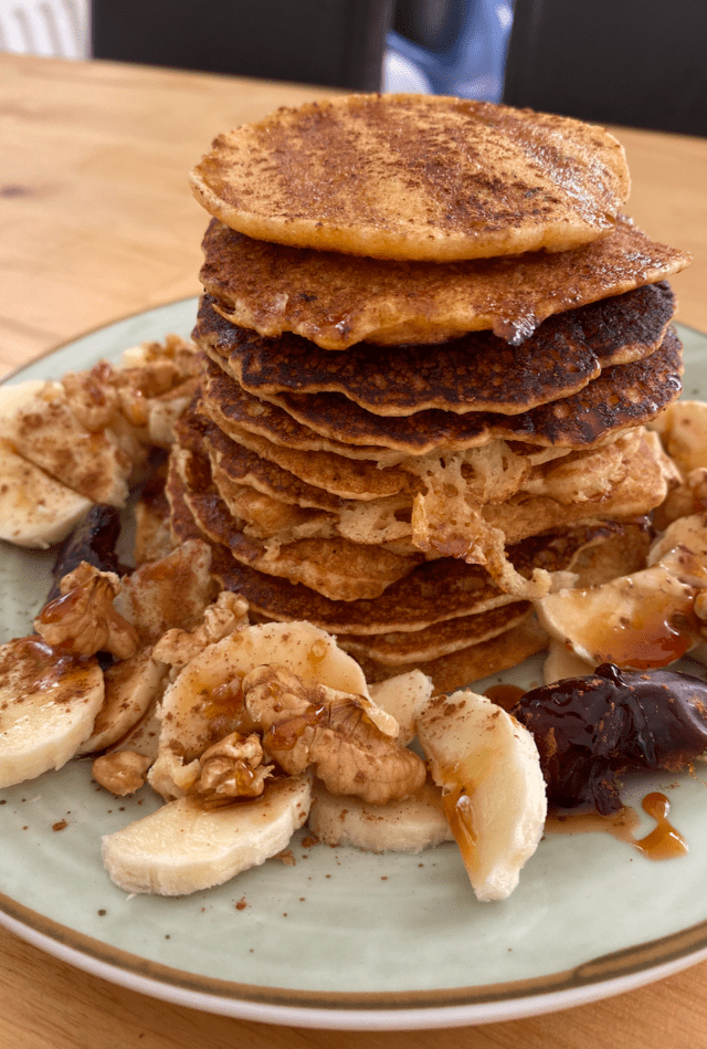 A stack of pancakes with bananas and walnuts on a plate.