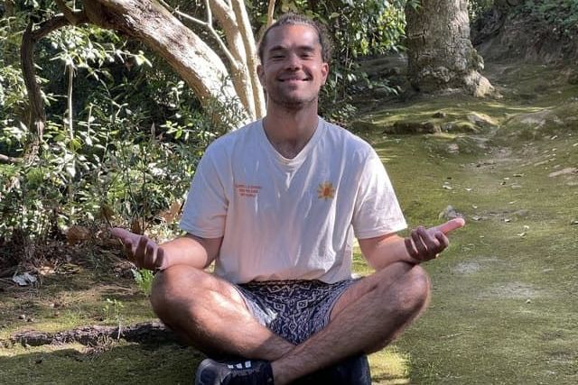 A man is sitting in a lotus position in the woods.