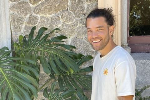 A man in a white t-shirt is standing in front of a monstera plant.