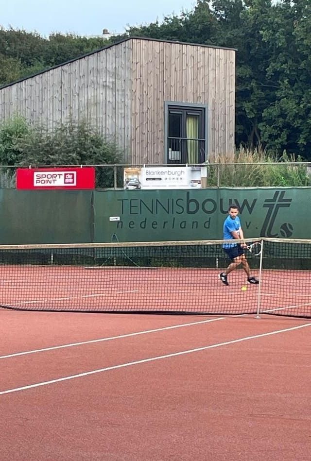 A man is playing tennis on a tennis court.