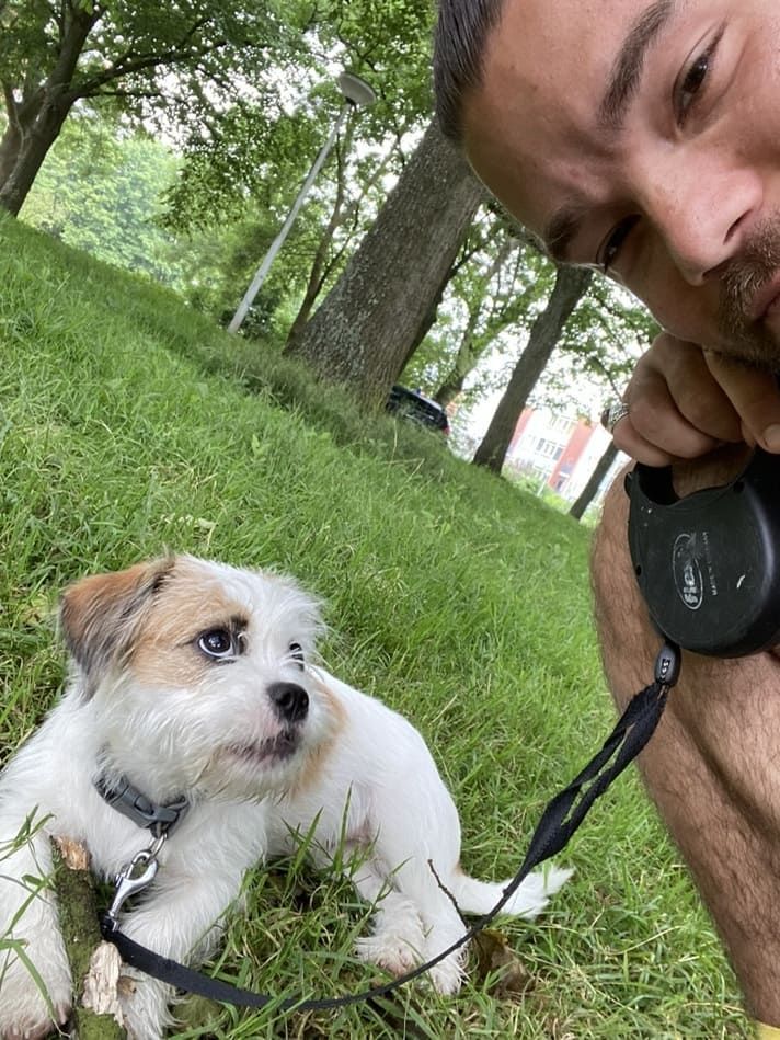 A man is standing next to a small dog on a leash.