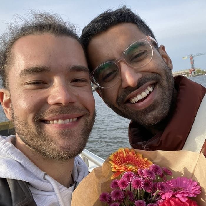 Two men are posing for a picture and one is holding a bouquet of flowers