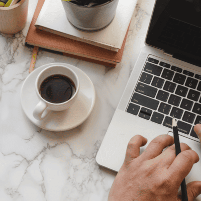 A person is typing on a laptop next to a cup of coffee