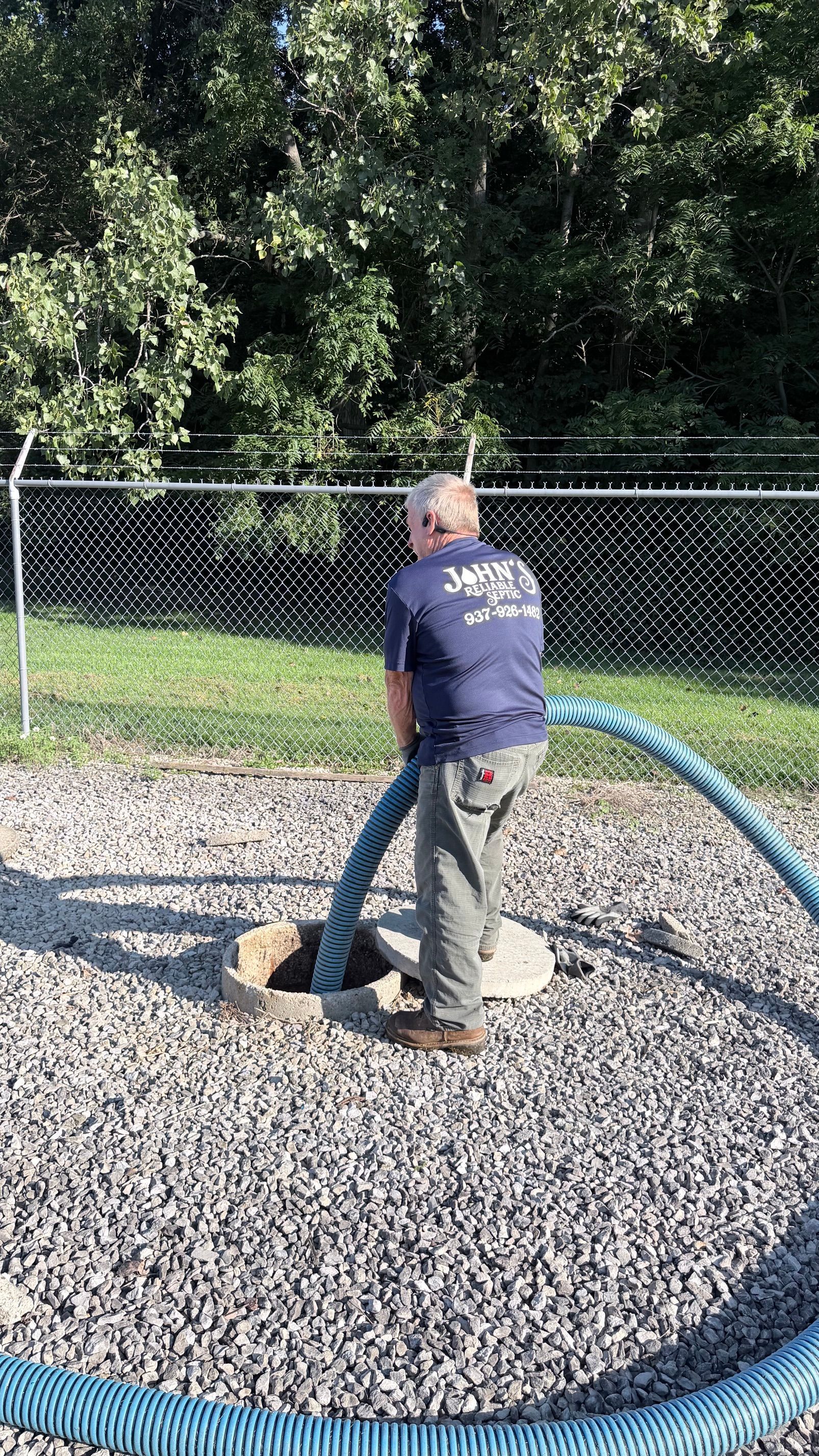 Utility worker inspecting an open lawn sewer access with a truck in the background