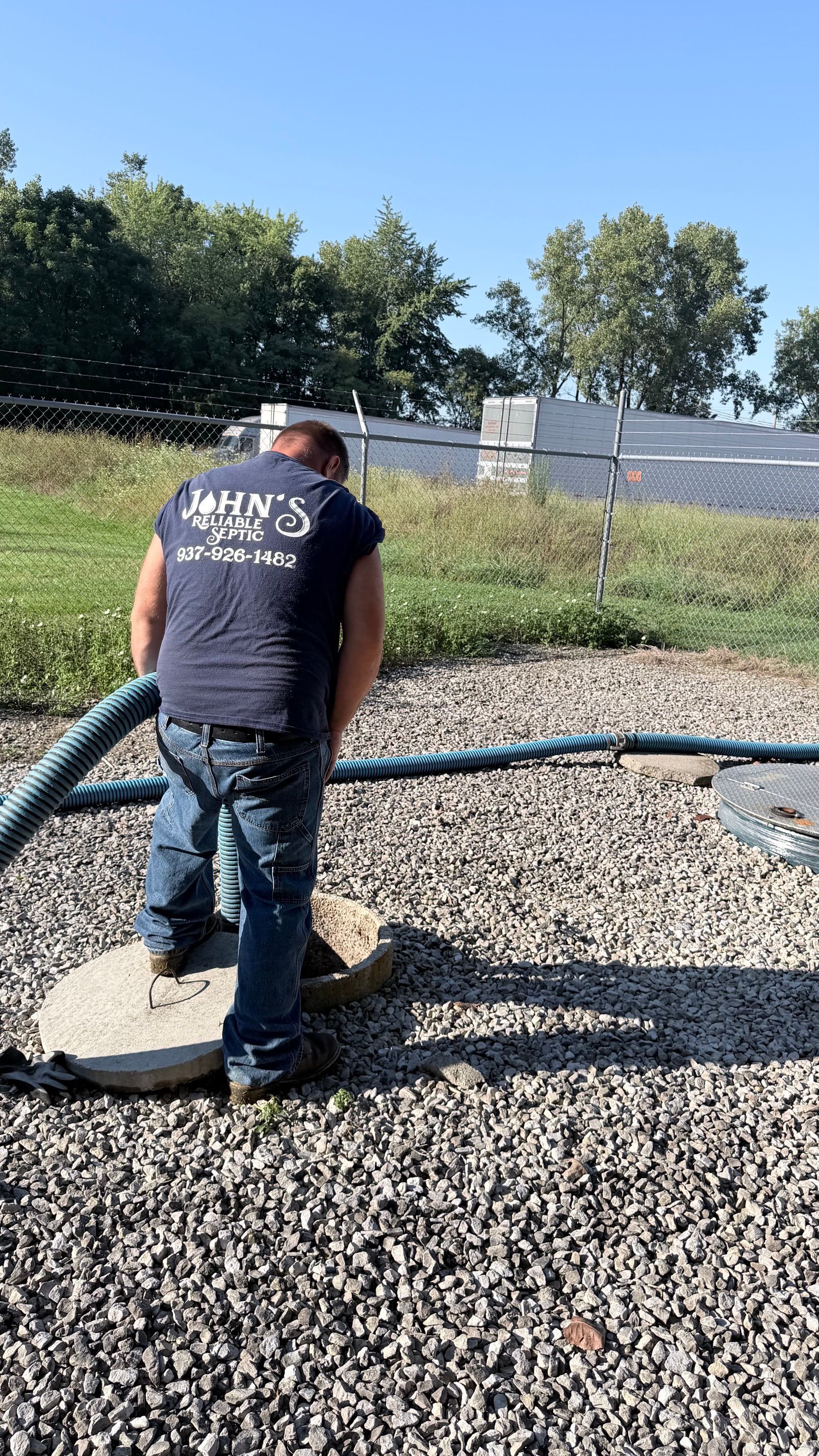 Worker cleaning a septic tank at night beside a house, with service truck and sign visible