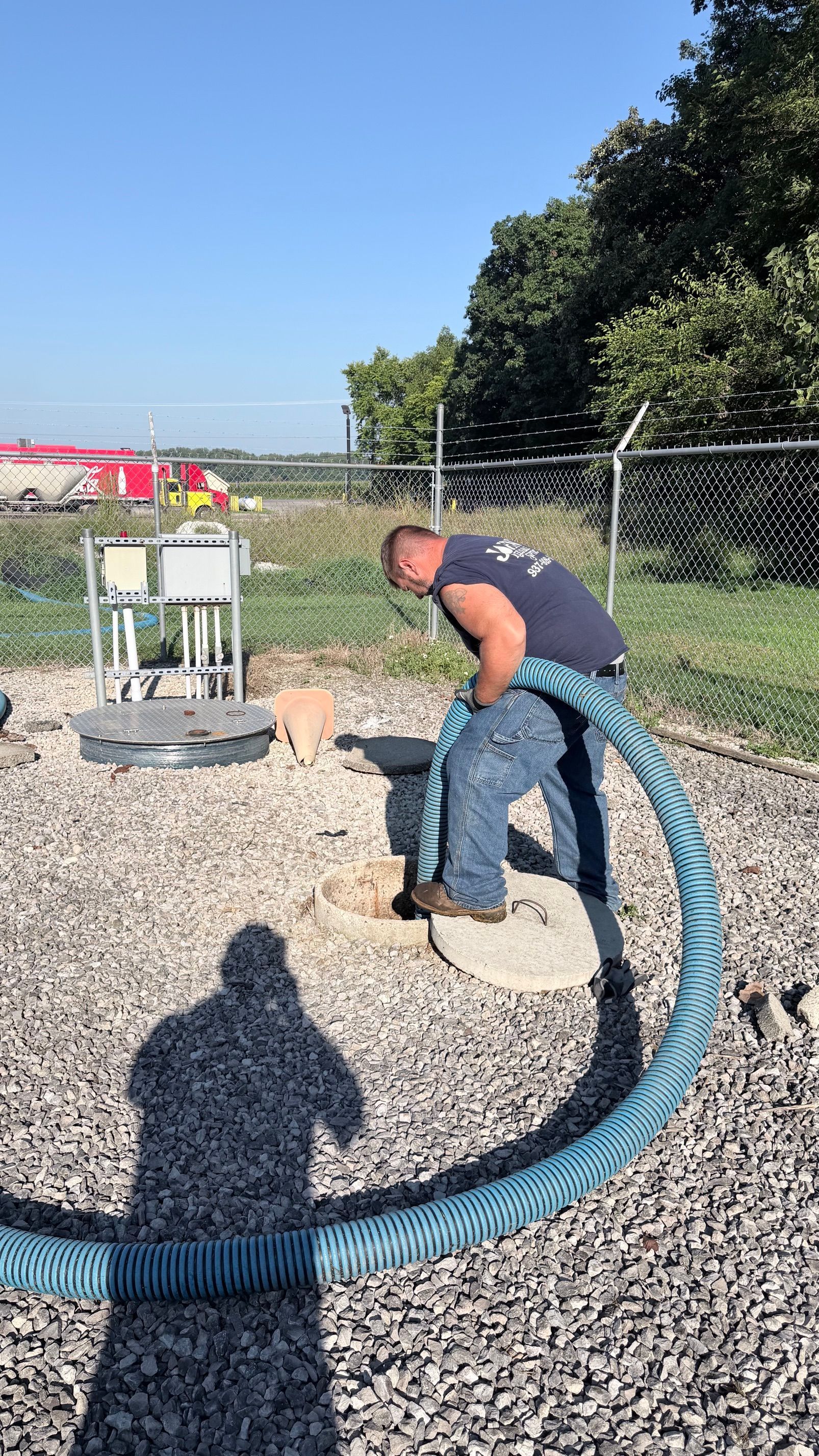 Worker in blue uniform vacuuming a sewer line on a suburban lawn next to a service truck.