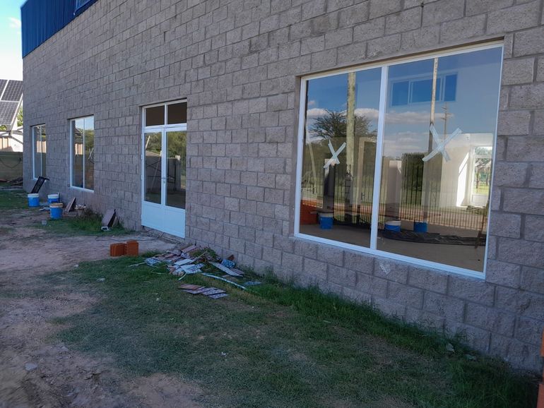 Edificio de piedra con grandes ventanales, una puerta blanca y césped irregular en la fachada.