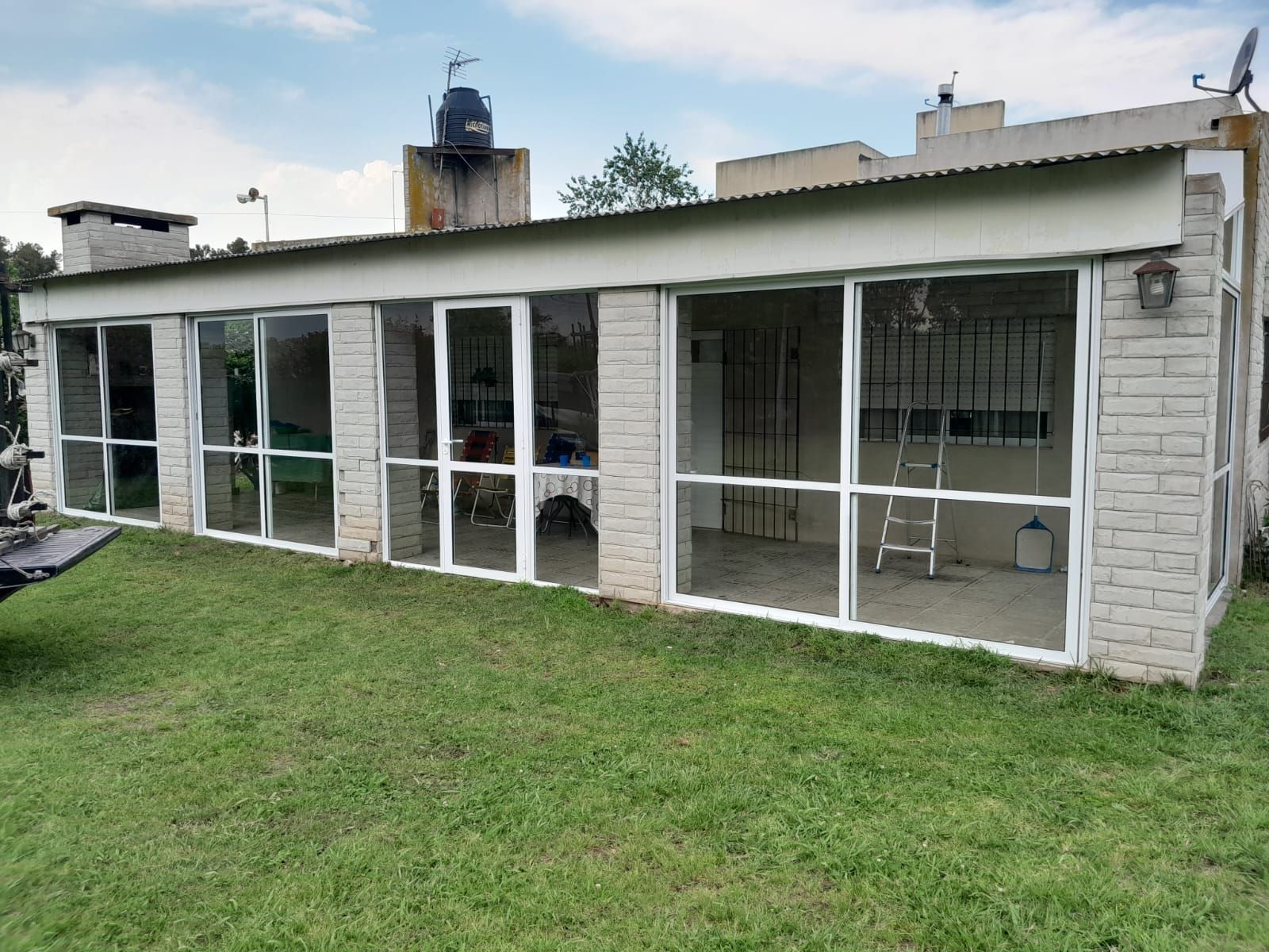 Casa moderna con paredes de cristal, césped y muebles de patio.