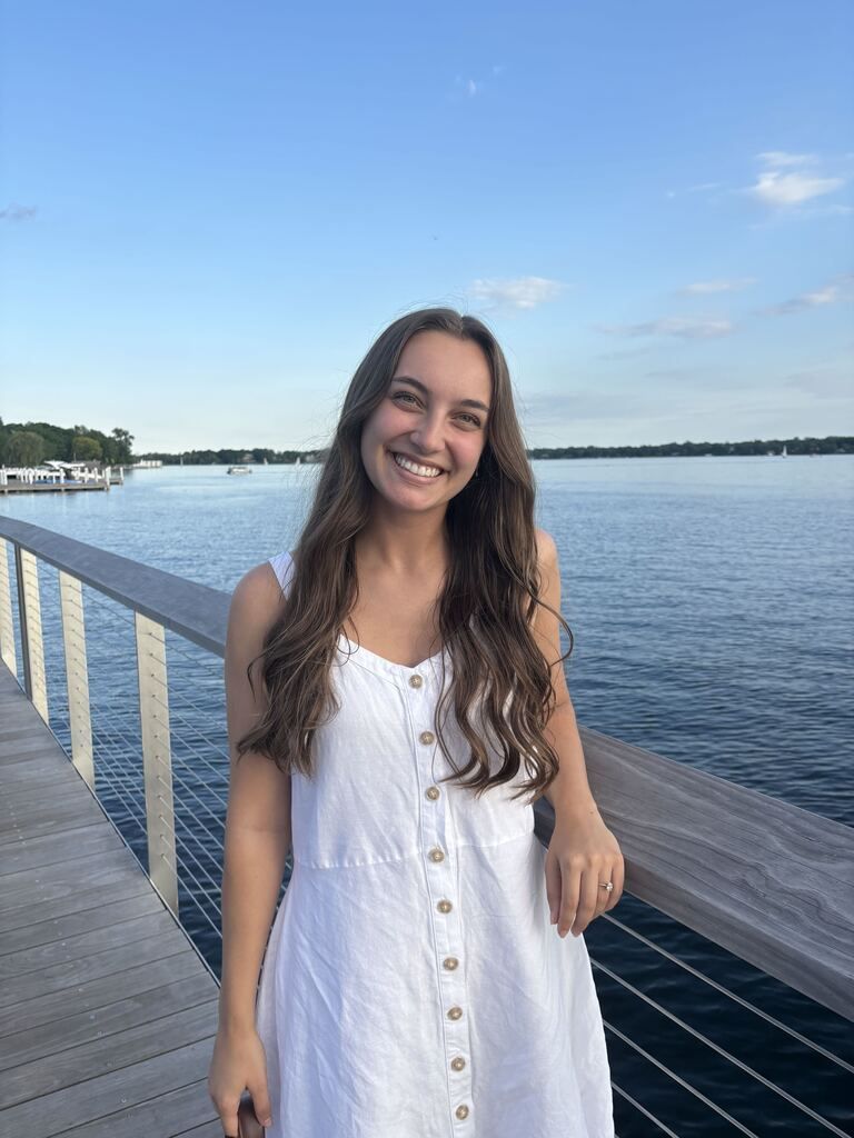Smiling woman in a white dress standing on a wooden pier by the water at sunset