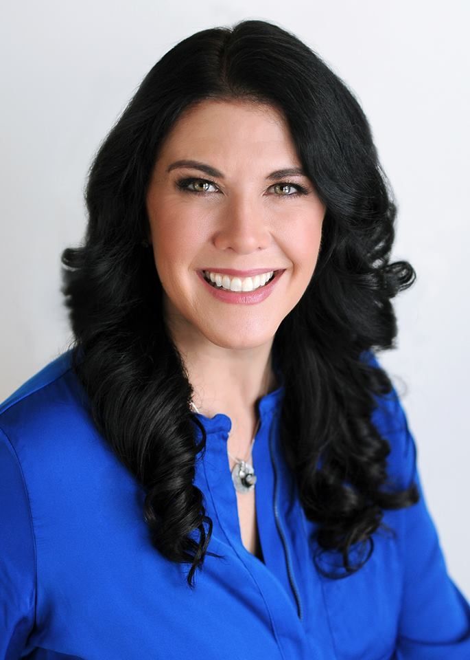 Smiling woman with long dark hair wearing a bright blue blouse against a white background