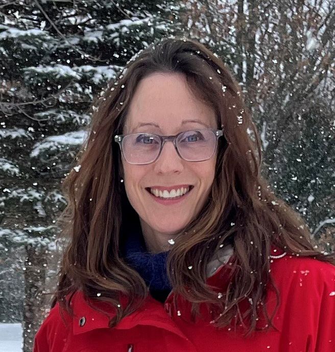 Smiling woman in glasses and a red coat standing outdoors in falling snow
