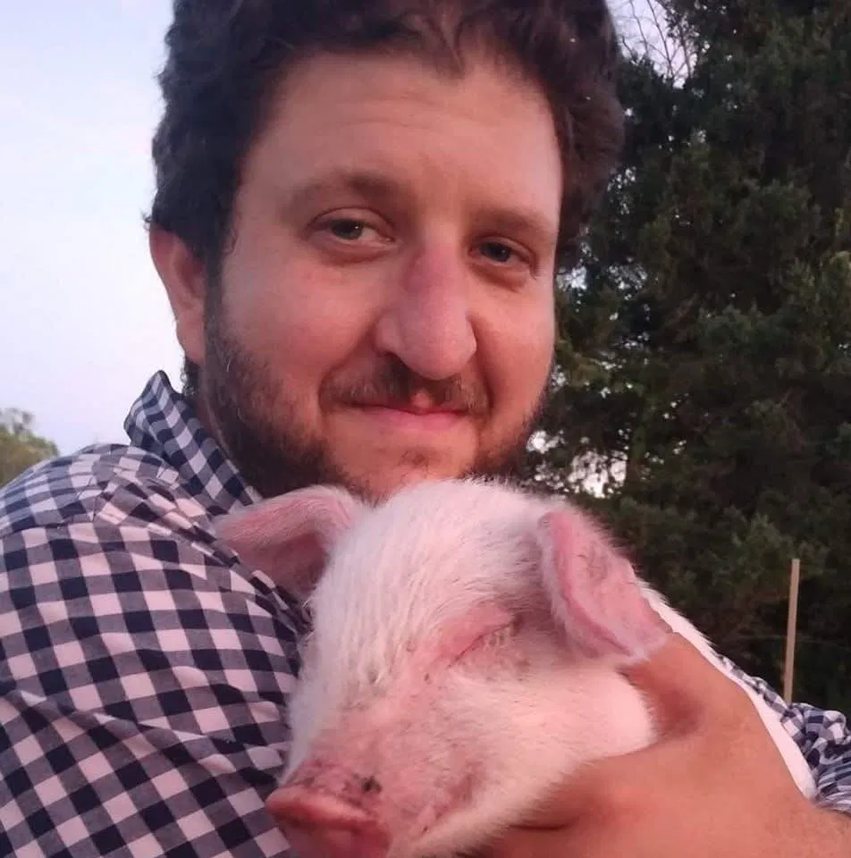 Man holding a sleeping pink piglet outdoors at dusk