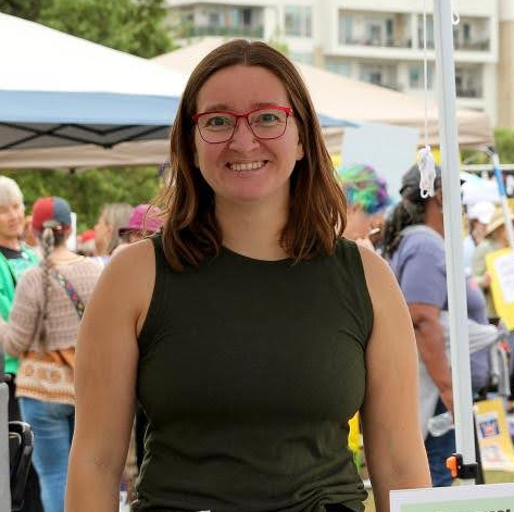 Smiling woman in red glasses and a dark green shirt at an outdoor market