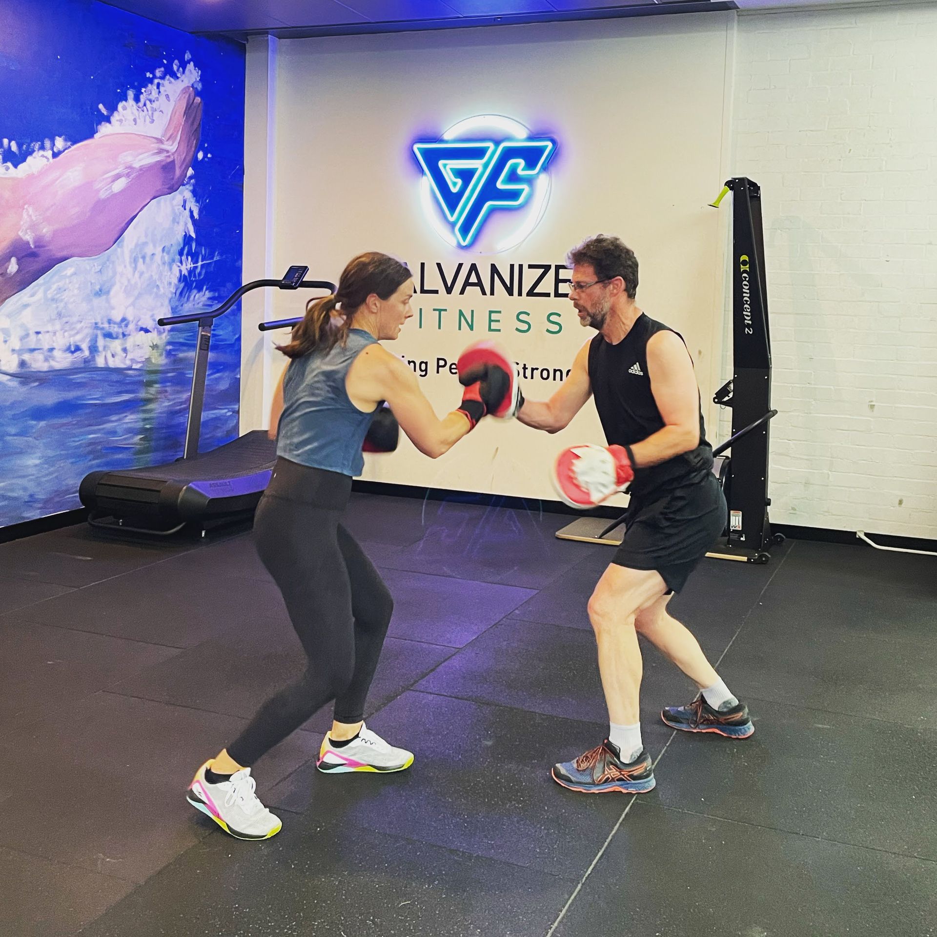 A man and a woman are boxing in a gym with a sign that says galvanize fitness