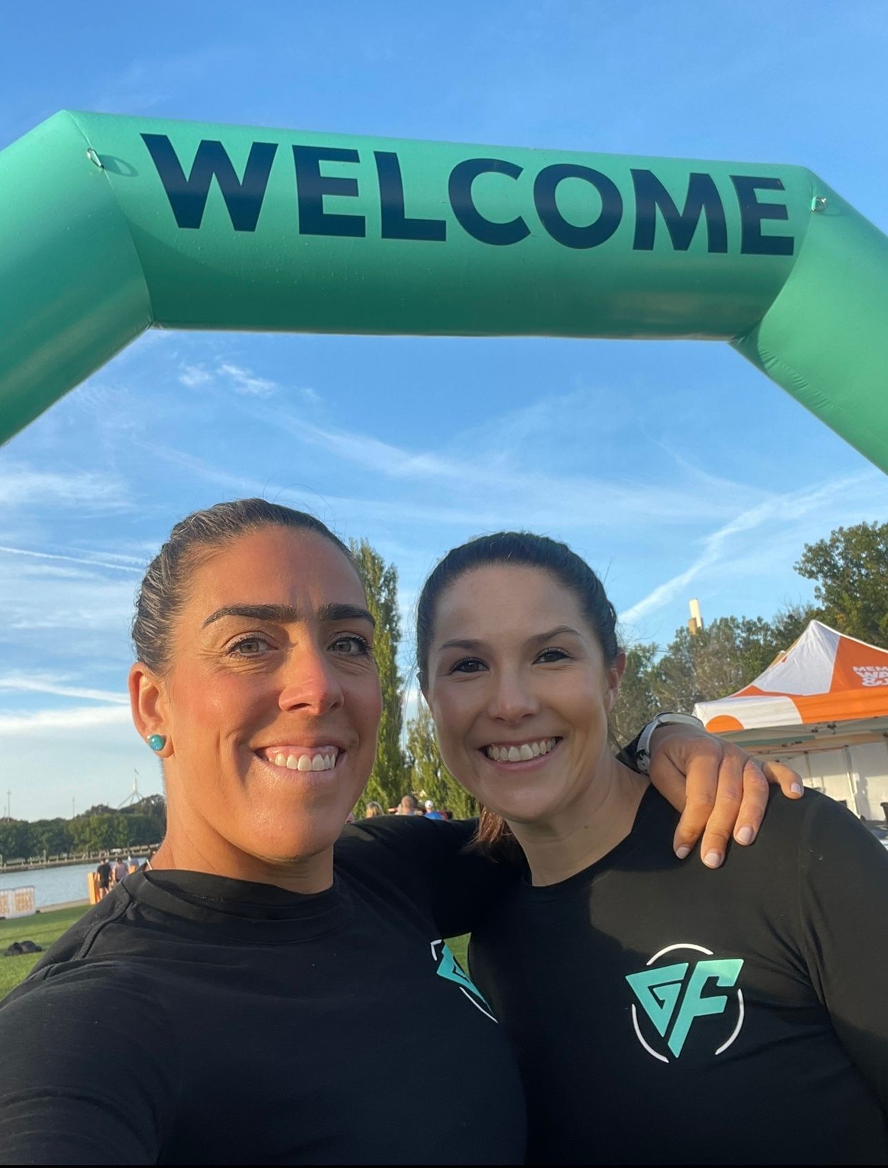 Two women are posing for a picture in front of an inflatable welcome sign.