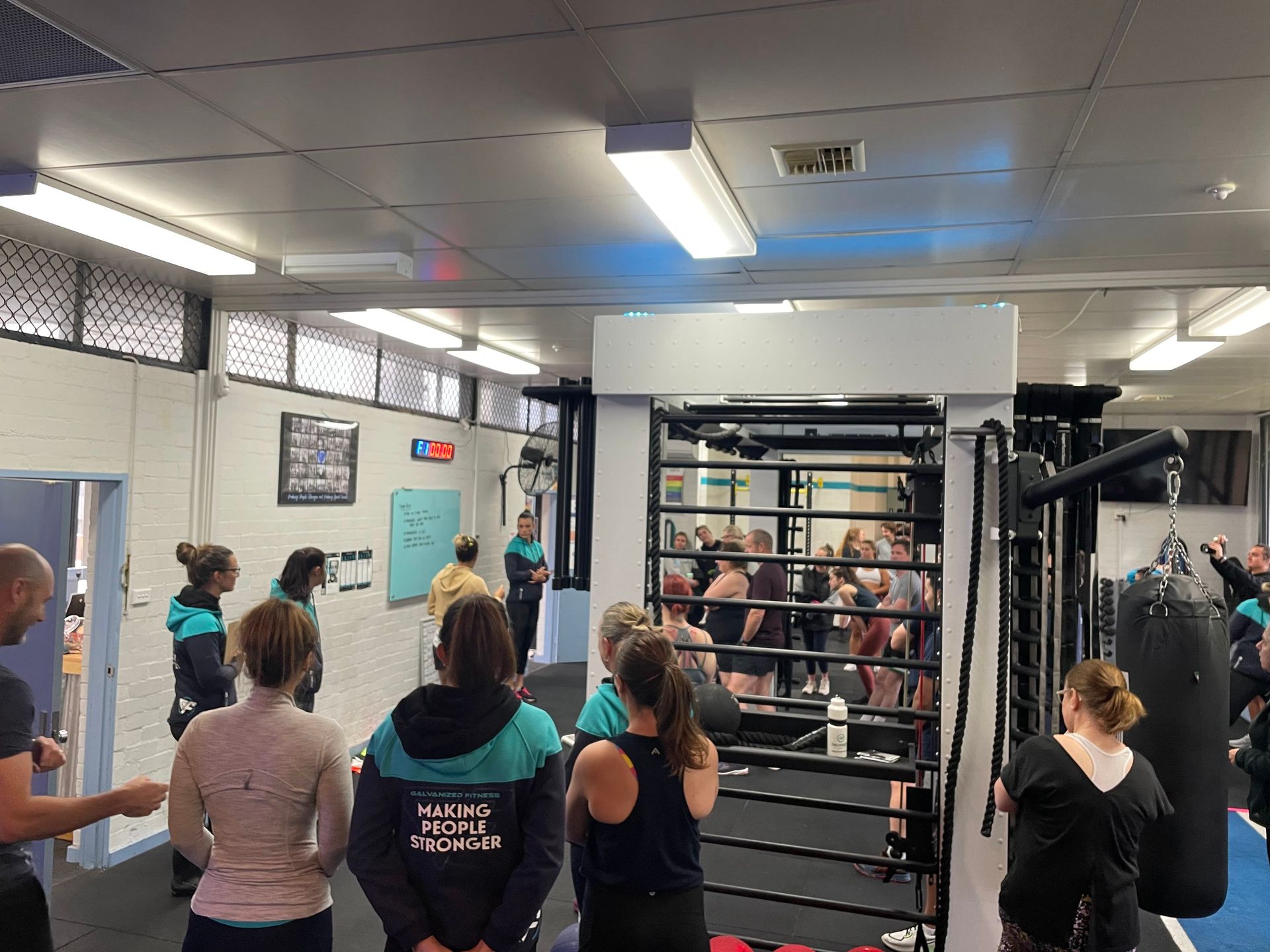People in a gym; some watching a boxing ring.  Various skin tones, clothing, and ages present.