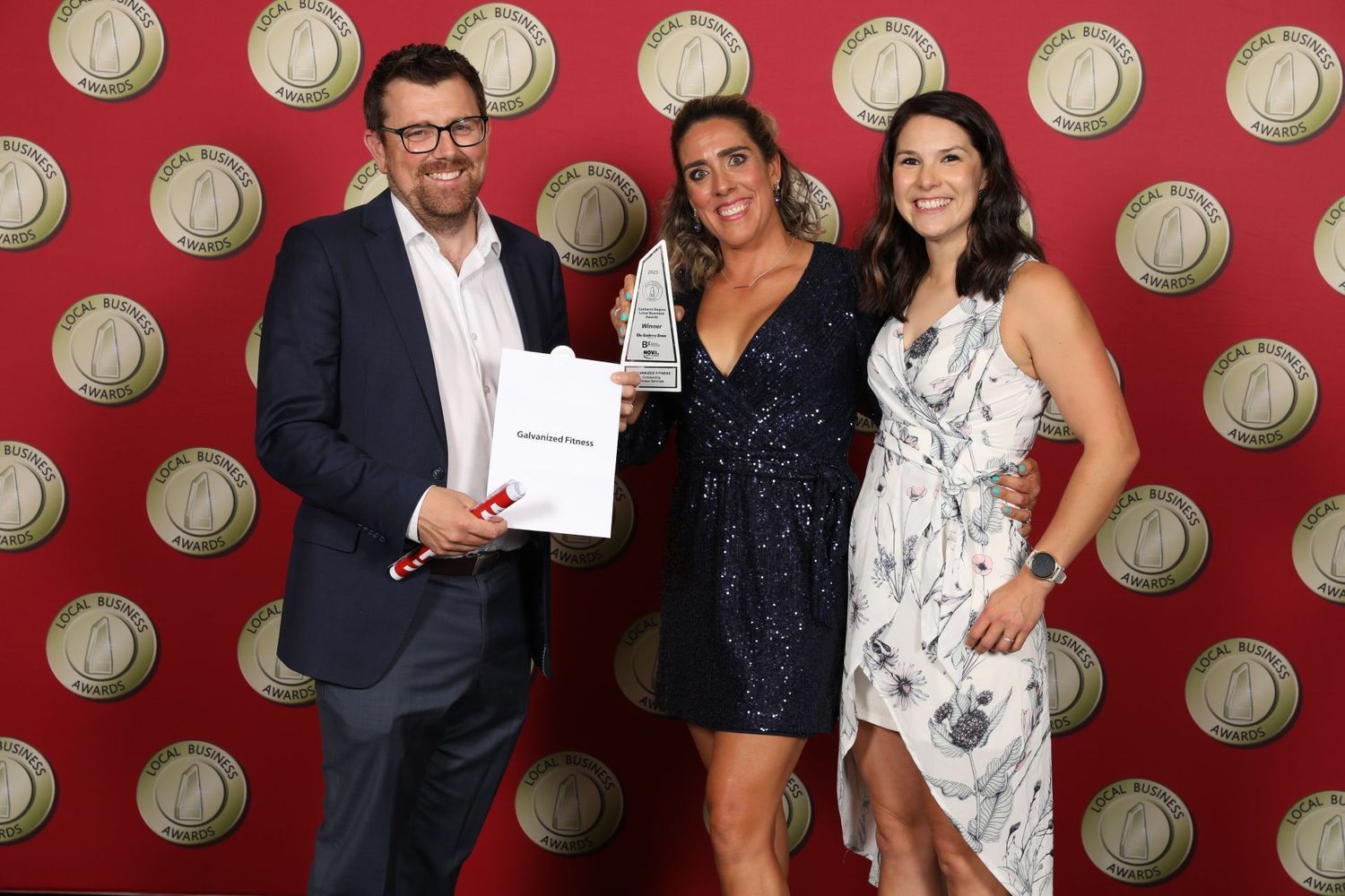 A man and two women are posing for a picture in front of a red wall.