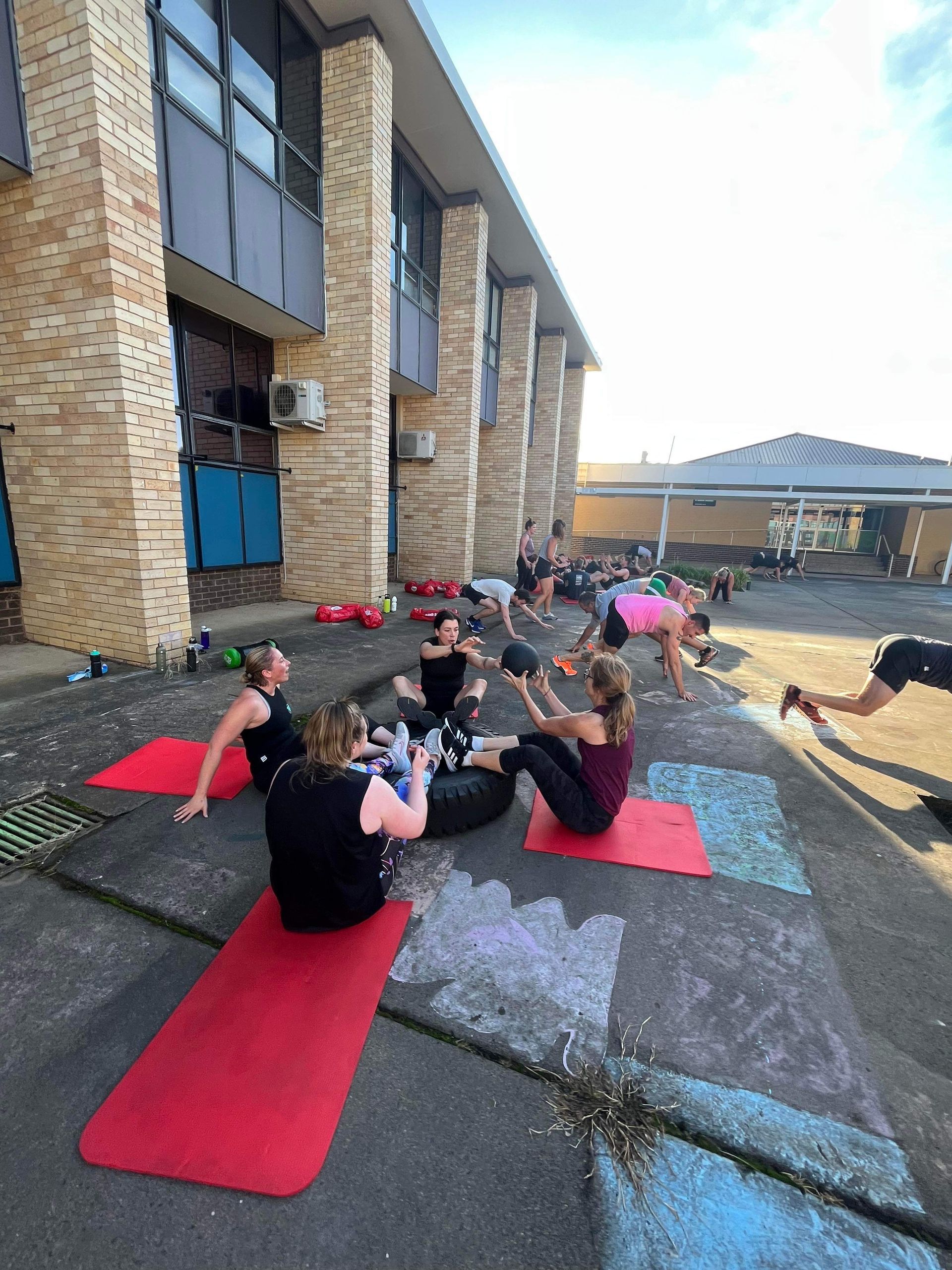 A group of people are sitting on red yoga mats outside of a building.