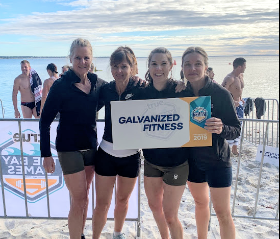 A group of women are standing on a beach holding a sign that says galvanized fitness.