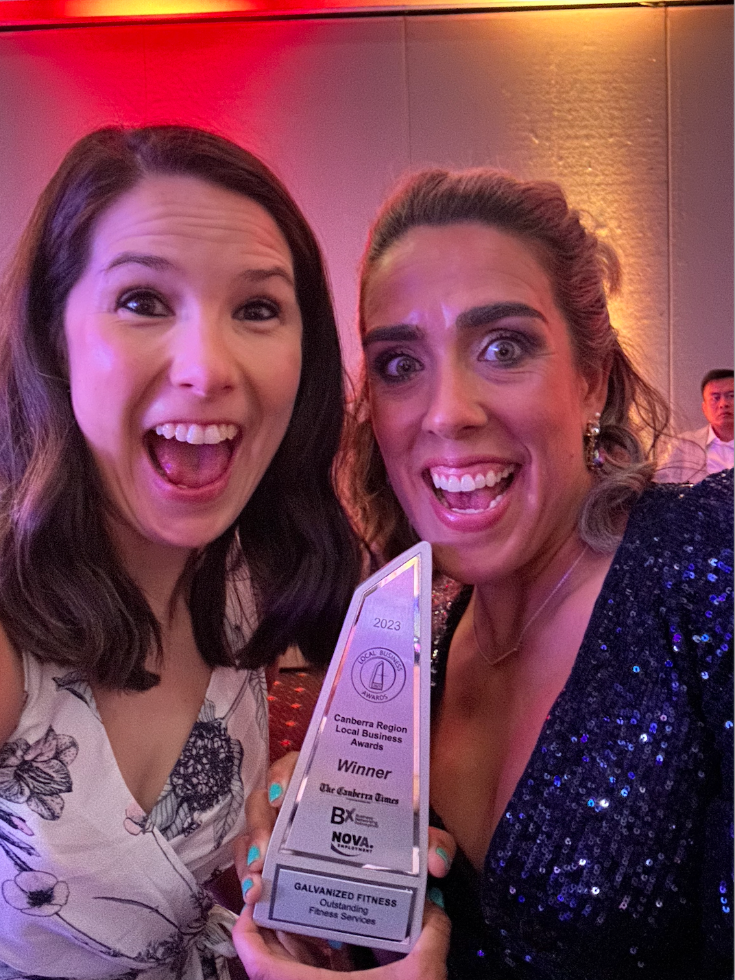 Two women are posing for a picture while holding a trophy.