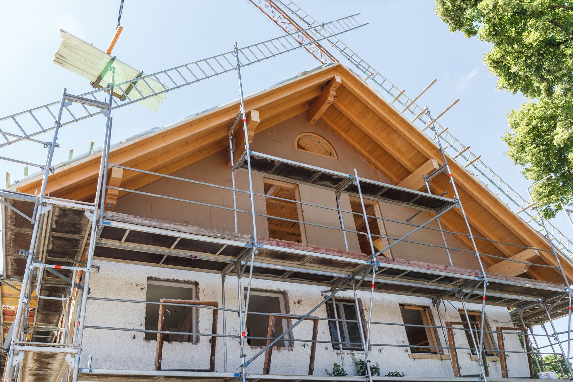 Haus im Bau mit Gerüst und Dachstuhl vor blauem Himmel