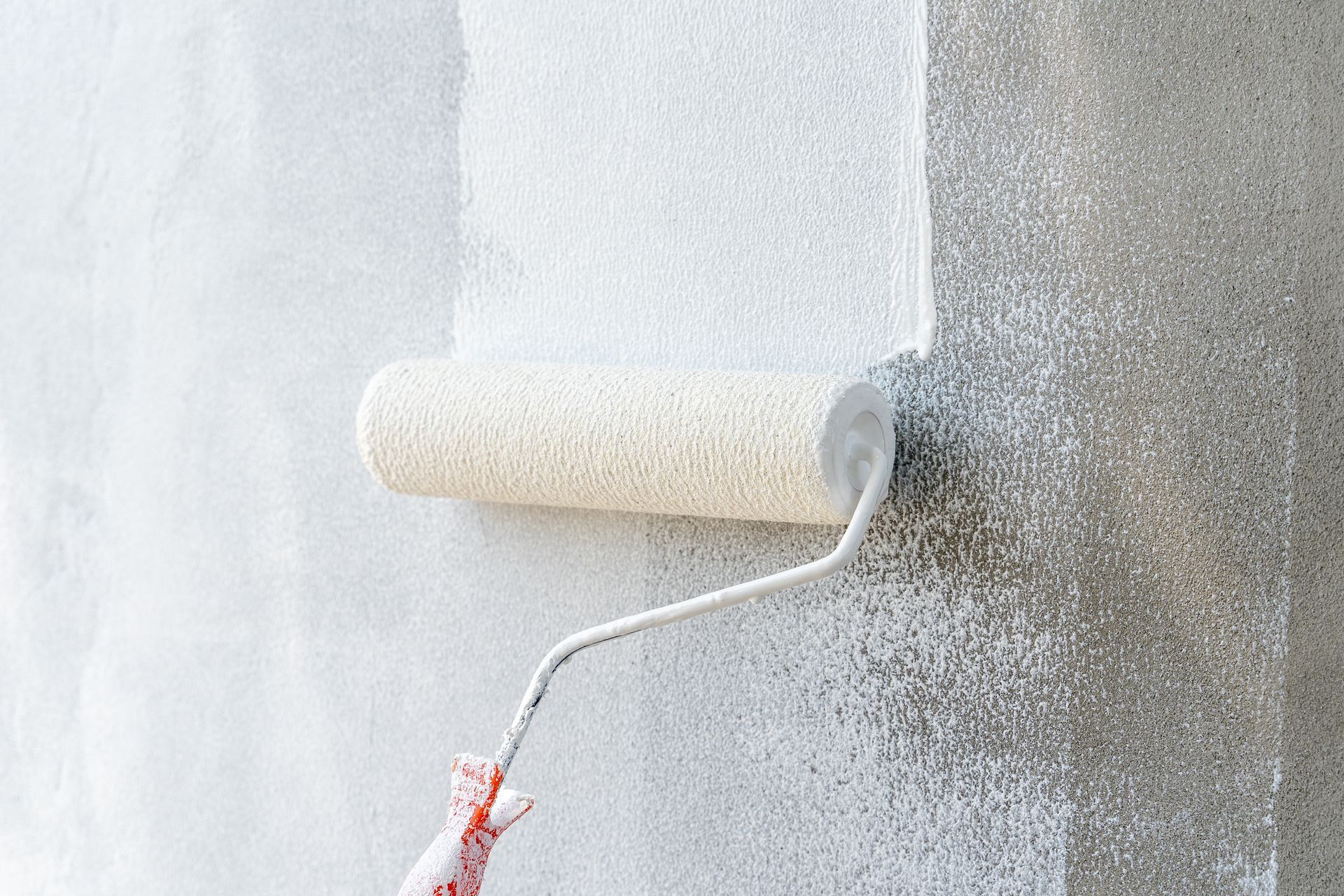 Eine Farbrolle trägt weiße Farbe auf eine graue Wand auf und schafft so einen frisch gestrichenen Bereich.