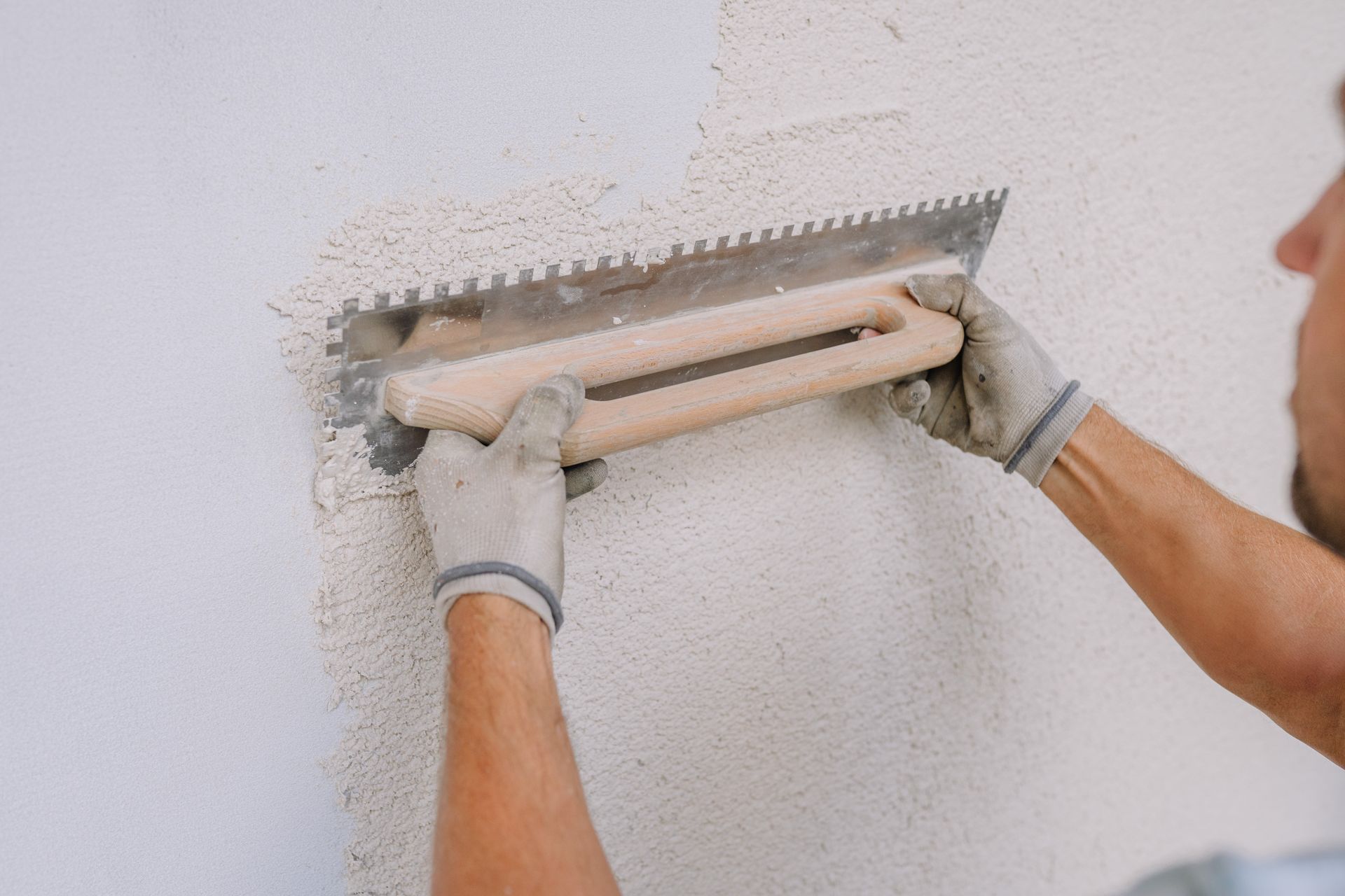 Ein Arbeiter glättet mit einer Kelle weißen Putz an einer Wand.
