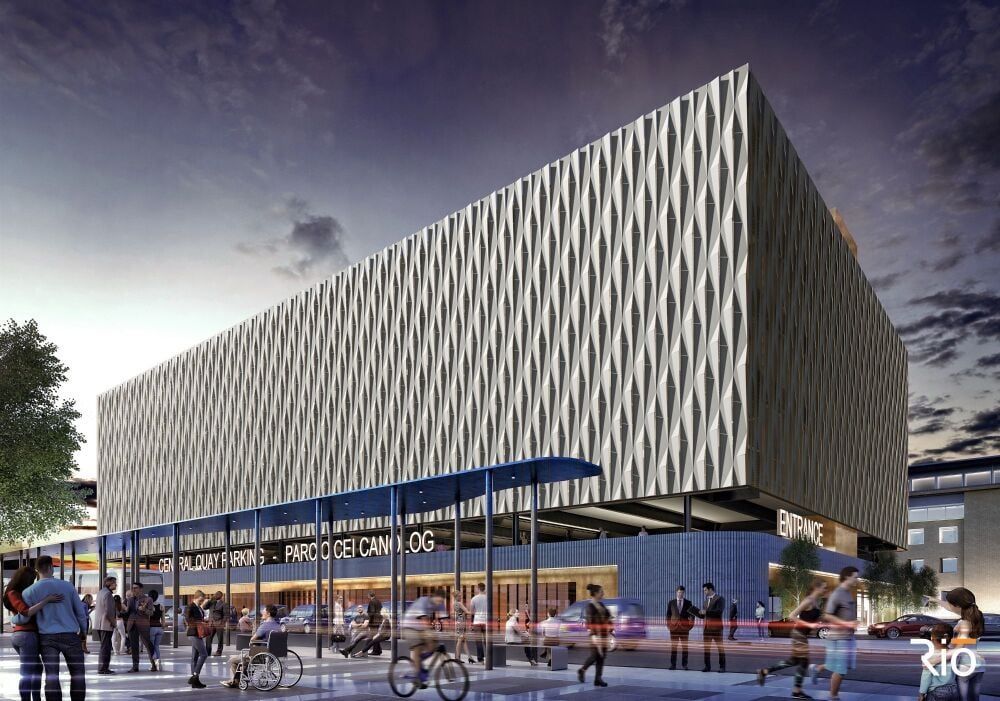 Modern building with textured facade. People gather near a covered entrance. Evening sky.