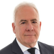 Older man in a suit looking at the camera, neutral expression, white background.