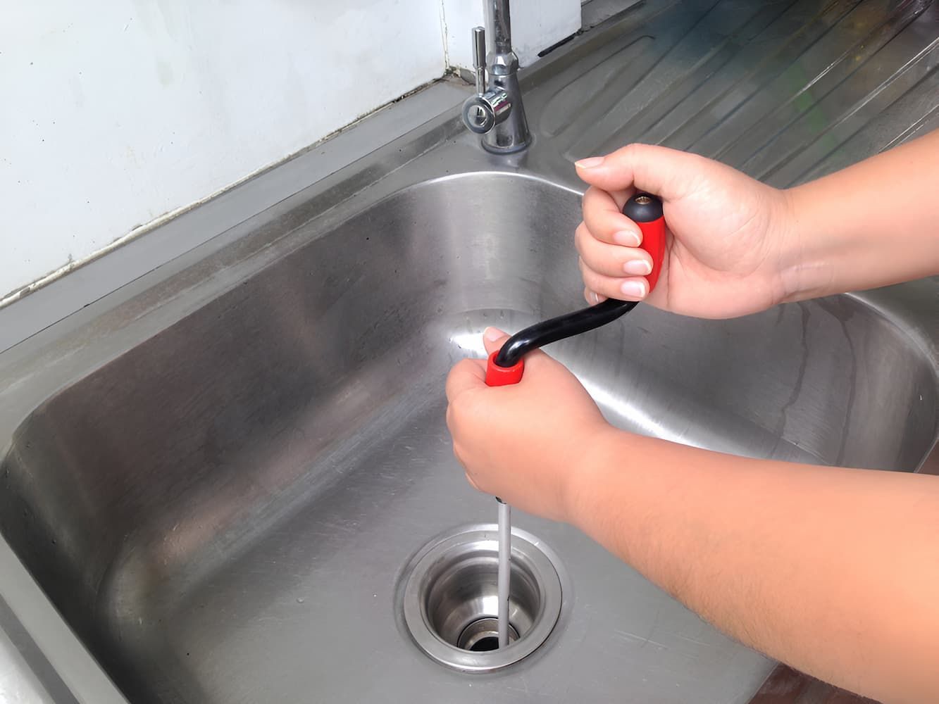 A Person Is Using A Snake To Drain A Sink — GPS Plumbing, Drainage & Gasfitting In Narromine, NSW