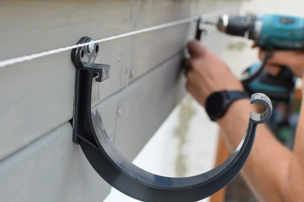 A Man Is Installing A Gutter With A Drill — GPS Plumbing, Drainage & Gasfitting In Dubbo, NSW