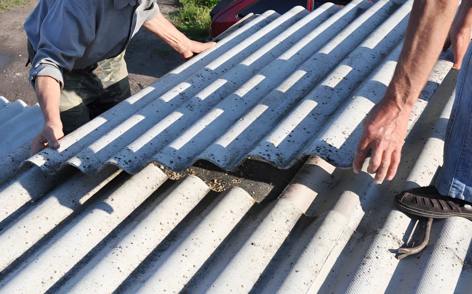 Two people placing a corrugated roofing sheet onto a roof.