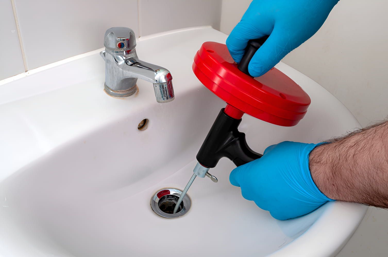 A Person Is Using A Drain Snake To Clean A Sink — GPS Plumbing, Drainage & Gasfitting In Dubbo, NSW