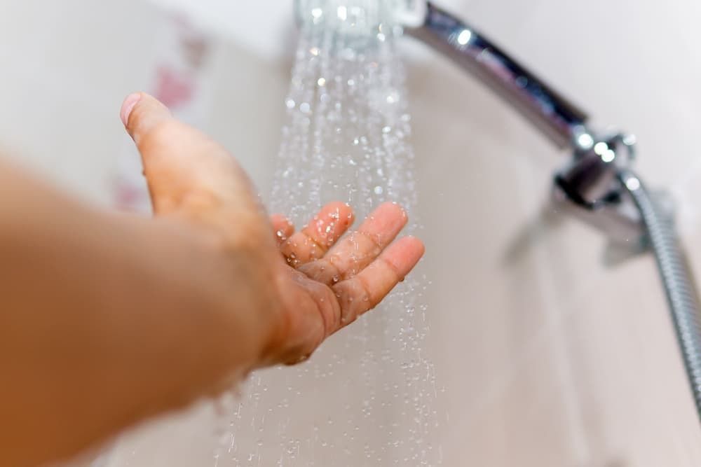 A Person Is Taking A Shower With Their Hand In The Water — GPS Plumbing, Drainage & Gasfitting In Dubbo, NSW