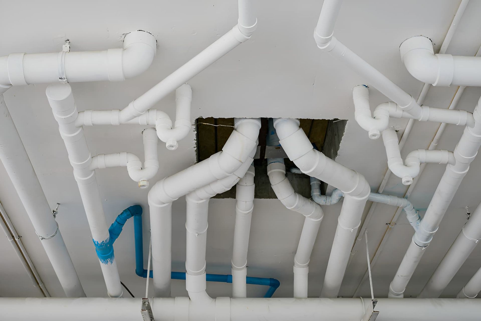 A Bunch Of White Pipes Are Hanging From The Ceiling Of A Building — GPS Plumbing, Drainage & Gasfitting In Wellington, NSW