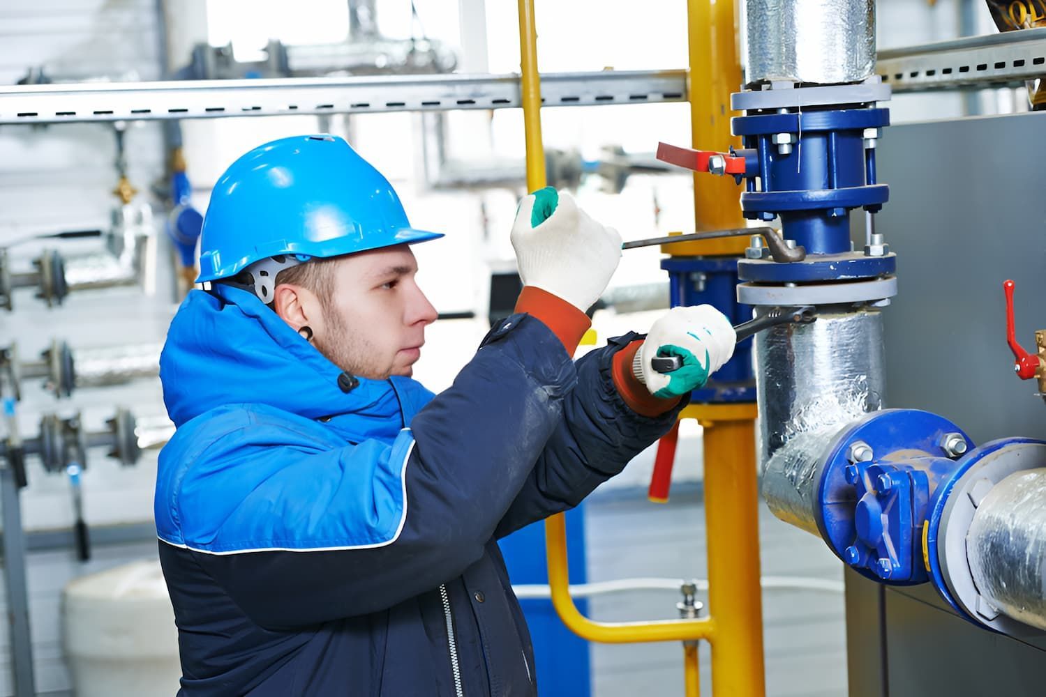 A Man In A Hard Hat Is Working On A Pipe In A Factory — GPS Plumbing, Drainage & Gasfitting In Dubbo, NSW