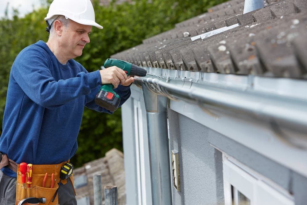 A Man Is Installing A Gutter On The Roof Of A House — GPS Plumbing, Drainage & Gasfitting In Dubbo, NSW