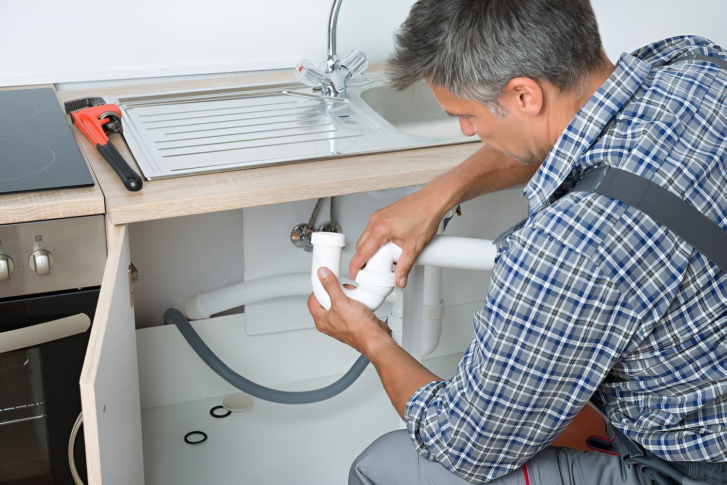 A Plumber Is Fixing A Sink In A Kitchen — GPS Plumbing, Drainage & Gasfitting In Narromine, NSW