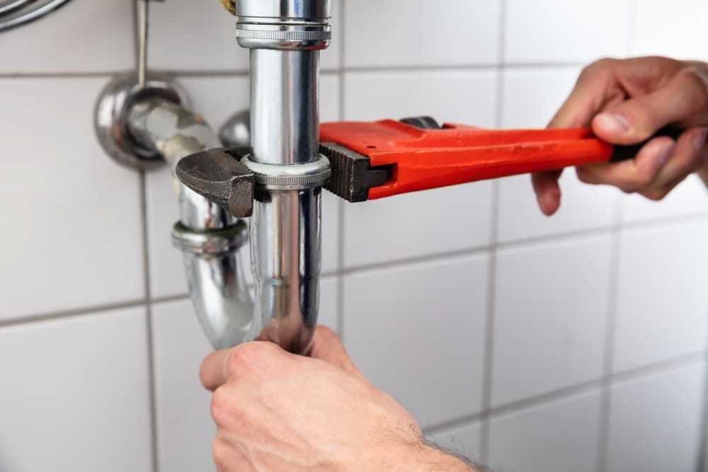 A Person Uses a Red Wrench to Tighten a Pipe Under a Sink