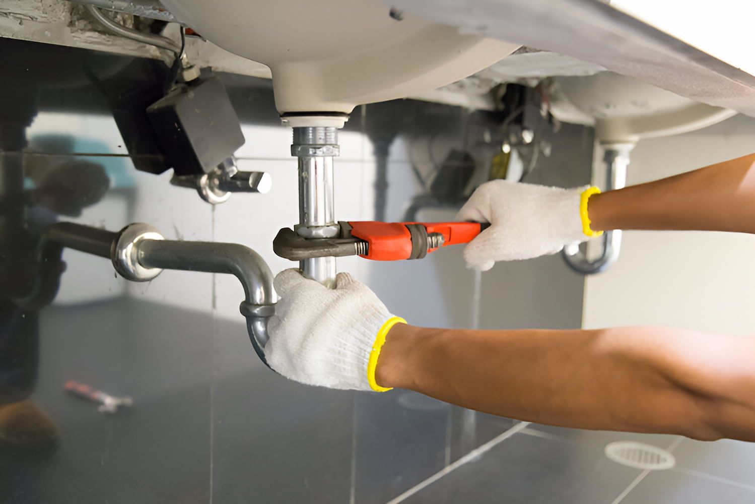 Hands using a wrench to tighten plumbing under a sink.