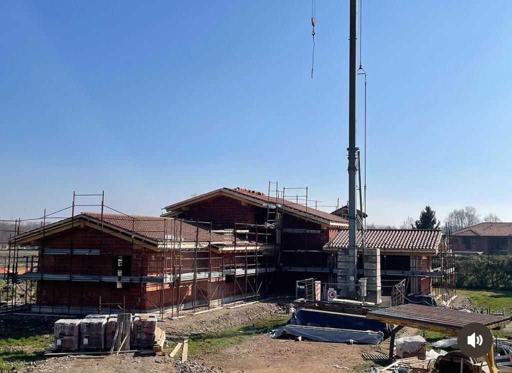 Casa in costruzione con muri in mattoni, impalcature e una gru contro il cielo azzurro.