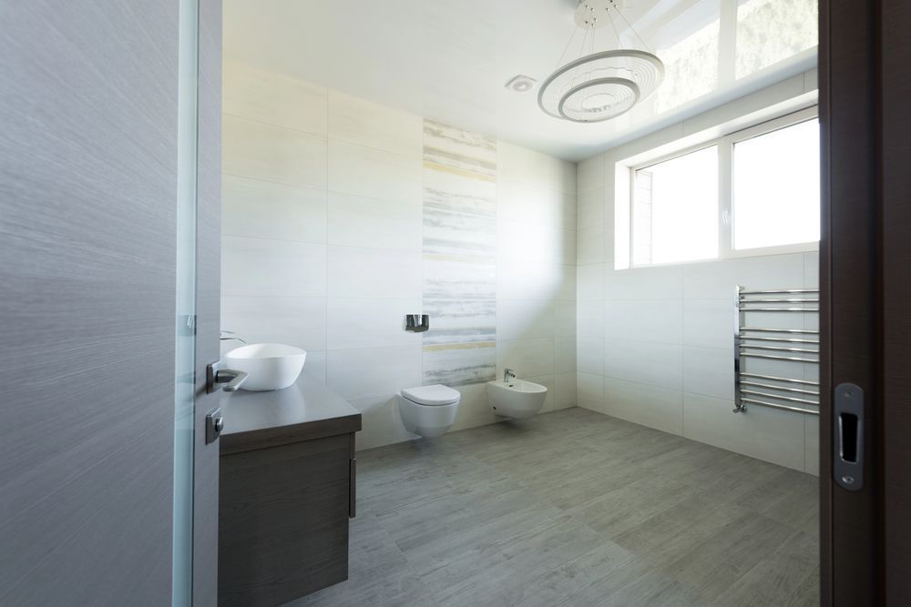 Bagno moderno con pavimento in piastrelle grigie, pareti bianche, WC, lavandino e portasciugamani.