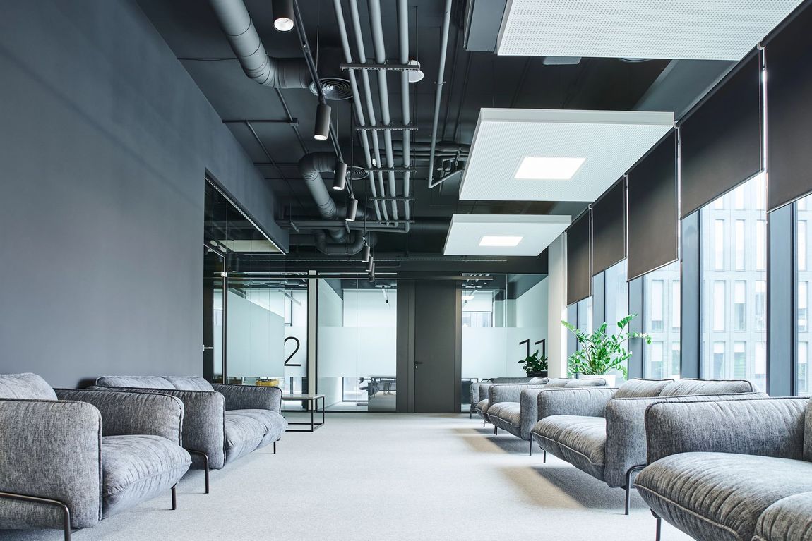 Moderna sala d'attesa con divani grigi, pareti in vetro e soffitto industriale.