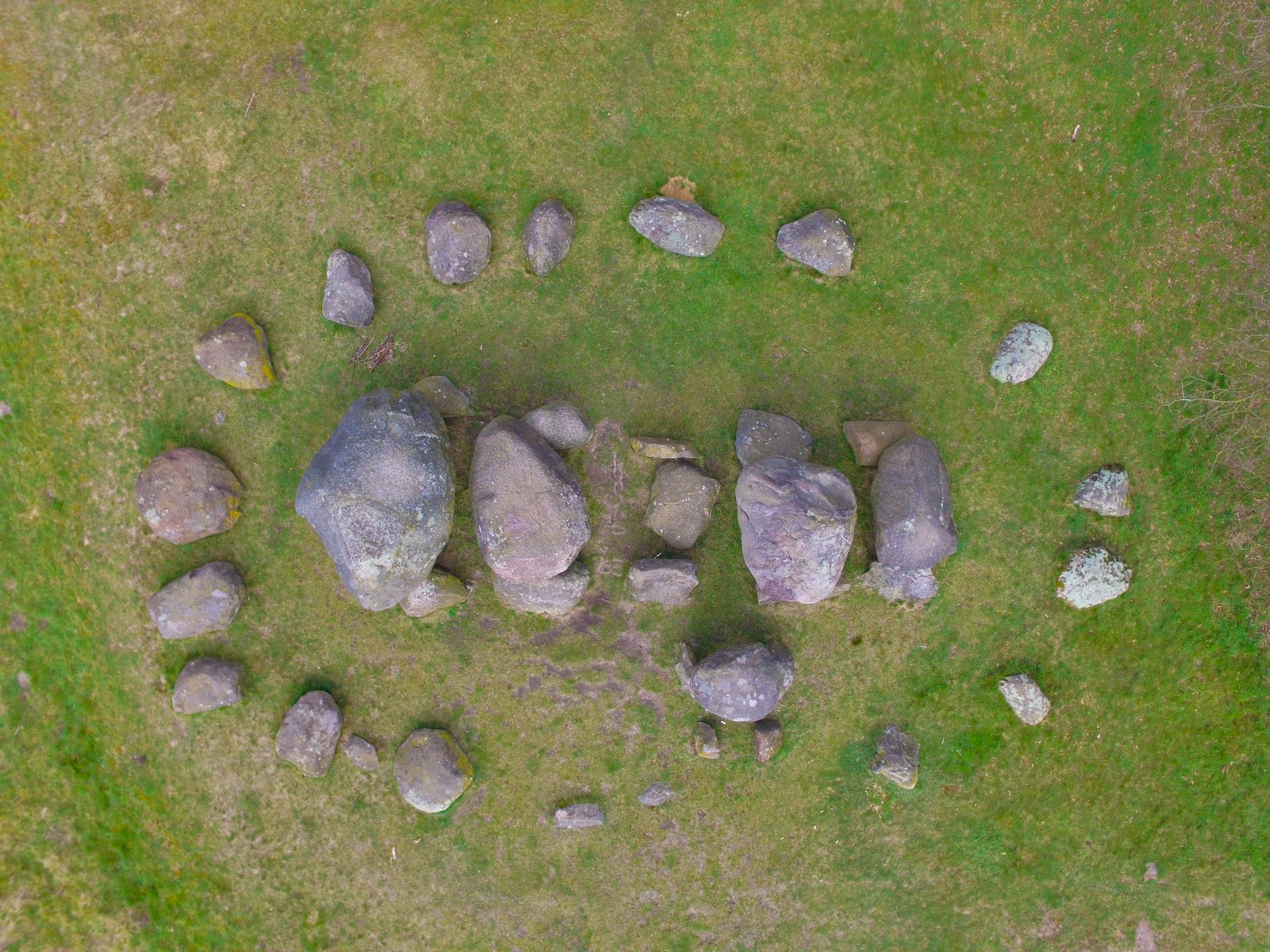 Een luchtfoto van een prehistorische steencirkel, met grote centrale rotsblokken omringd door een ring van kleinere stenen.