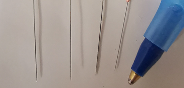 Vier dunne metalen draadjes naast een blauwe balpen op een witte ondergrond.